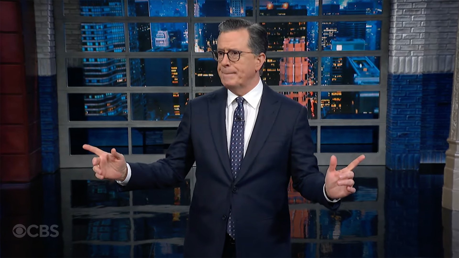 A man in a suit stands on a talk show stage.