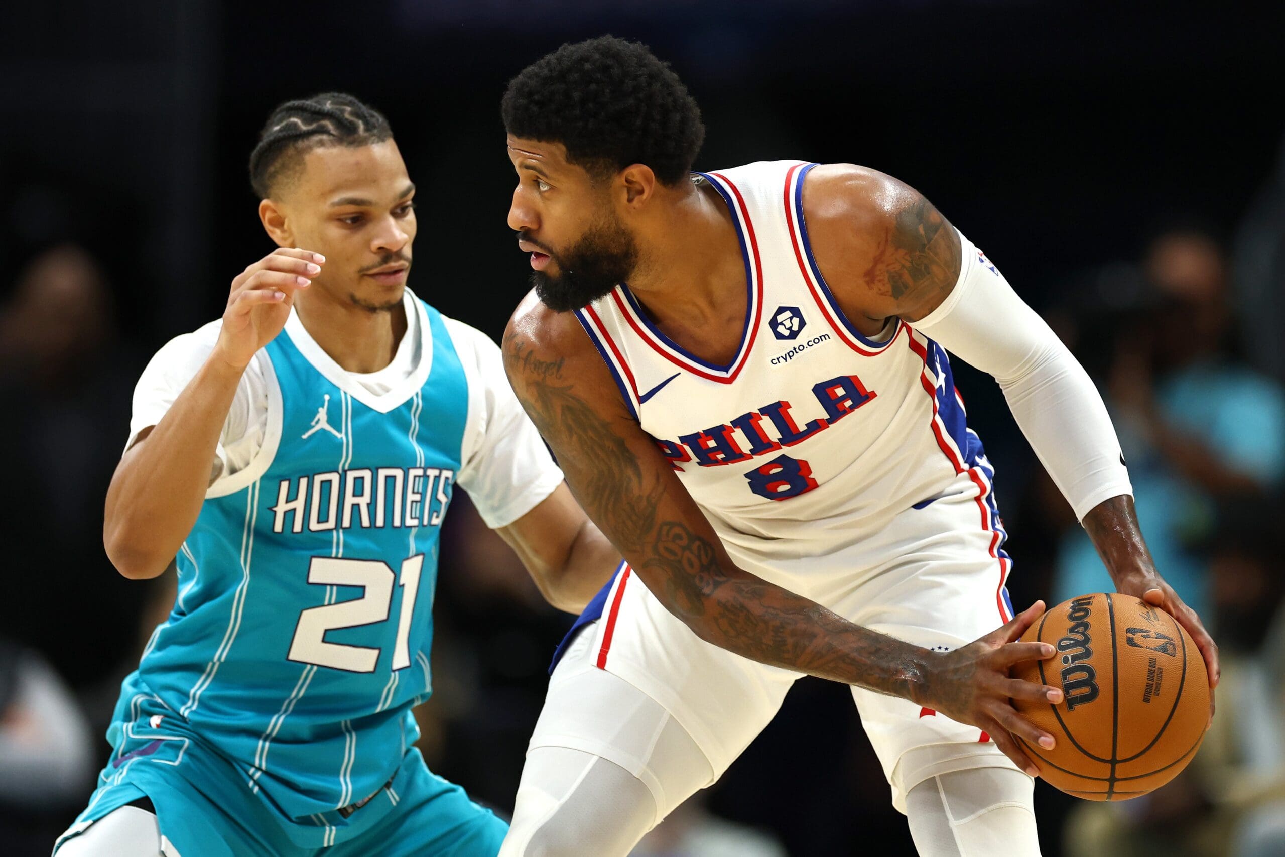 Paul George #8 of the Philadelphia 76ers looks over the court while defended by Isaiah Wong #21 of the Charlotte Hornets during the first half of the game at Spectrum Center on December 16, 2024 in Charlotte, North Carolina.