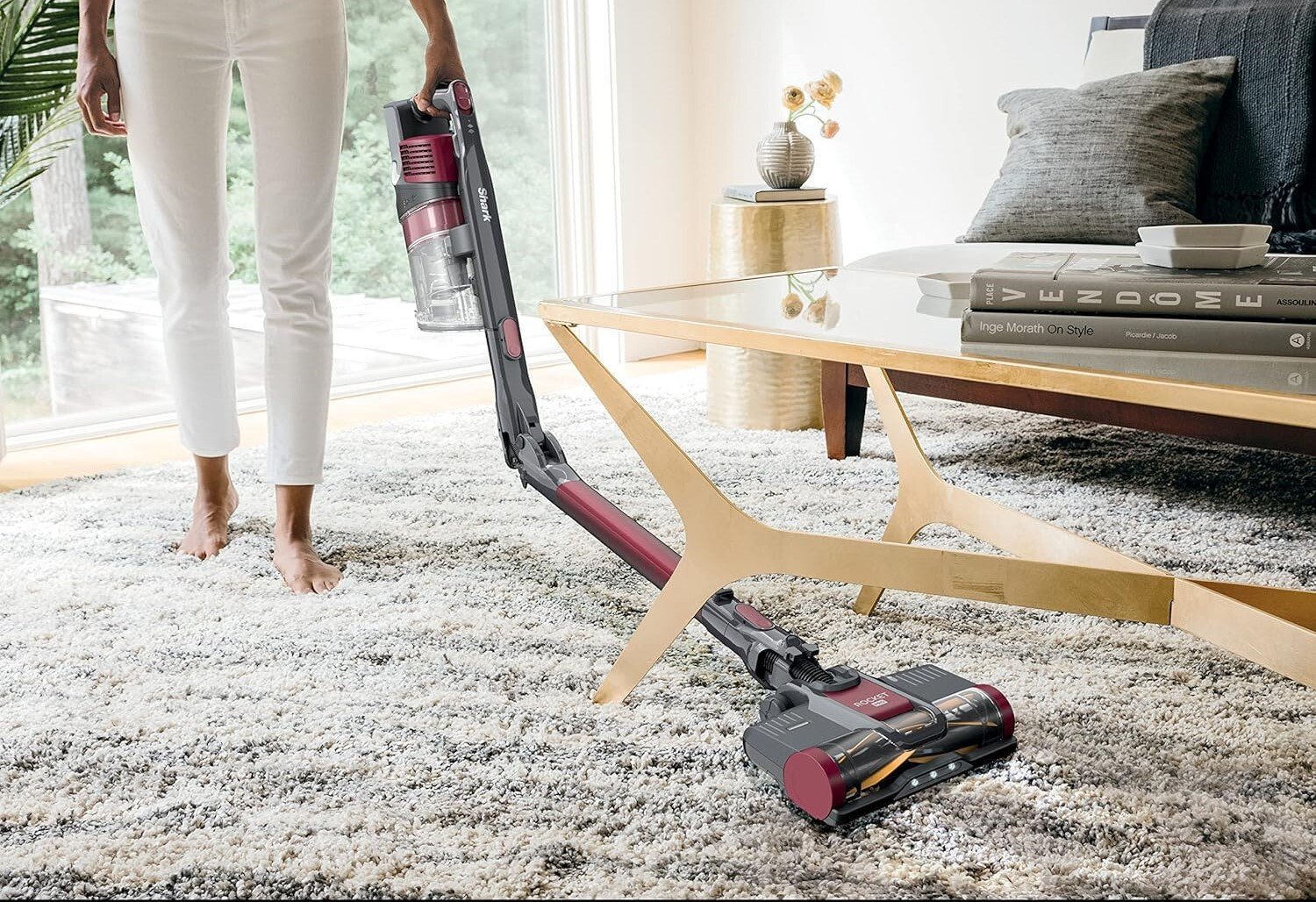 the shark pet plus cordless stick vacuum cleans under a coffee table on a grey colored carpet
