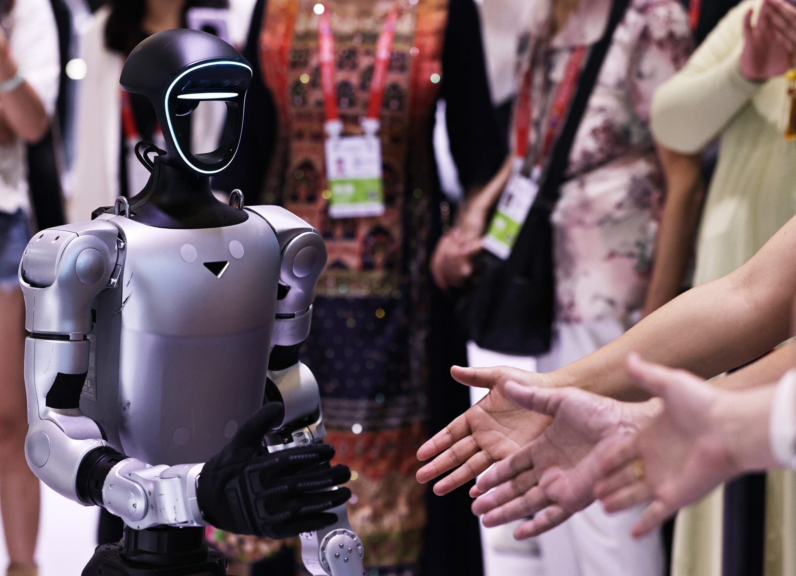 A short silver robot reaches out to shake a human's hand.
