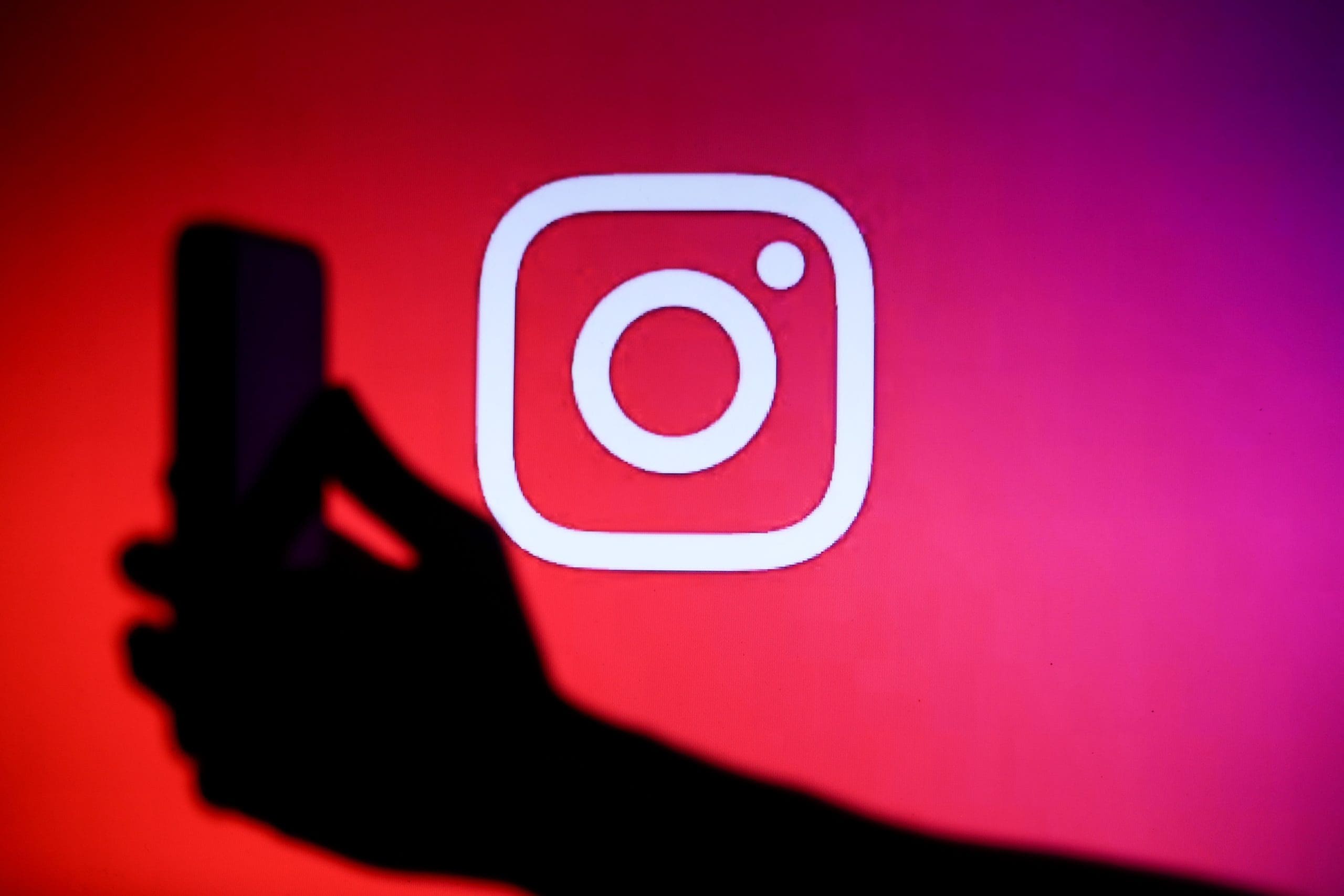 A hand holding a phone in front of a large Instagram logo.